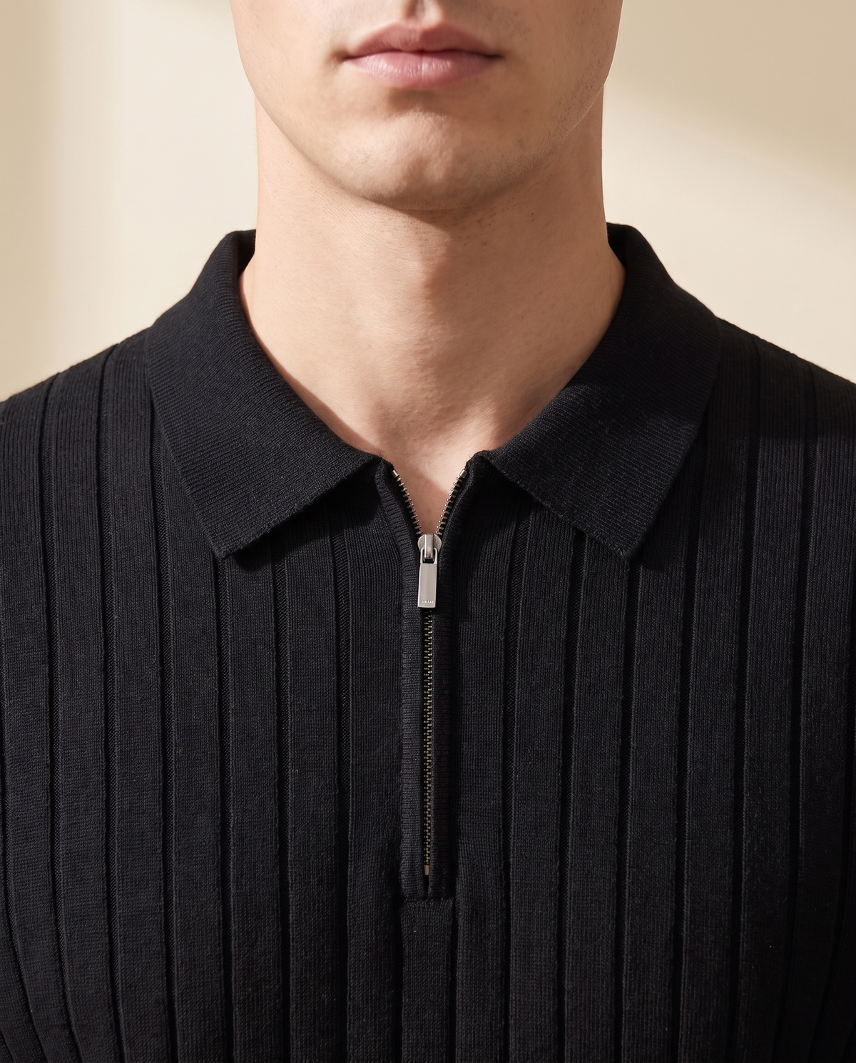 The Osborne ribbed zip polo in black, close-up of folded collar and silver zip